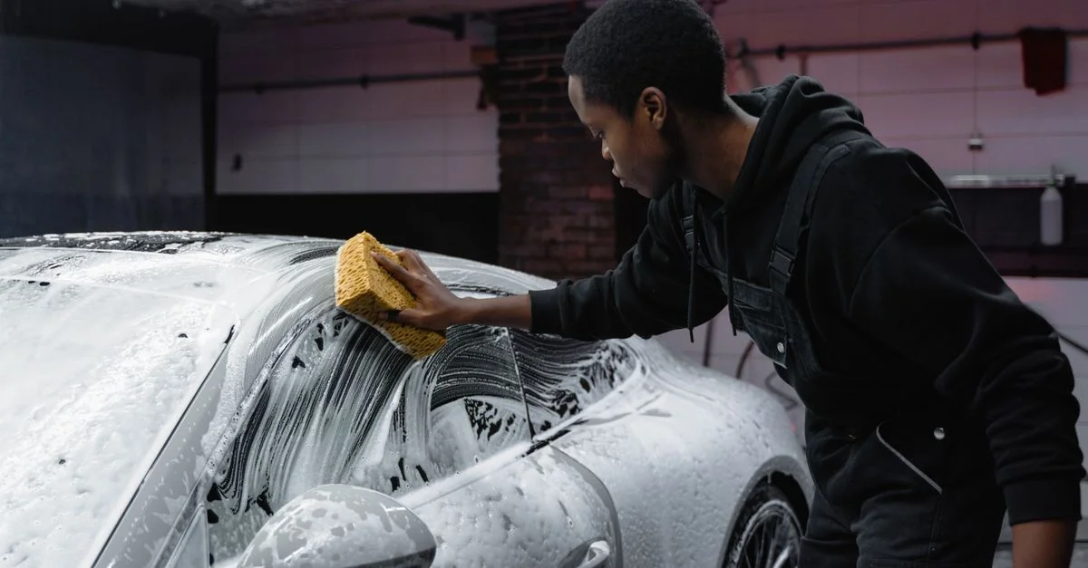 Un jeune homme nettoie une voiture de luxe avec une éponge dans un carwash intérieur.