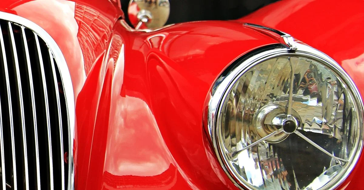 Un gros plan d'une voiture vintage rouge mettant en valeur ses détails en chrome brillant et ses phares distinctifs.