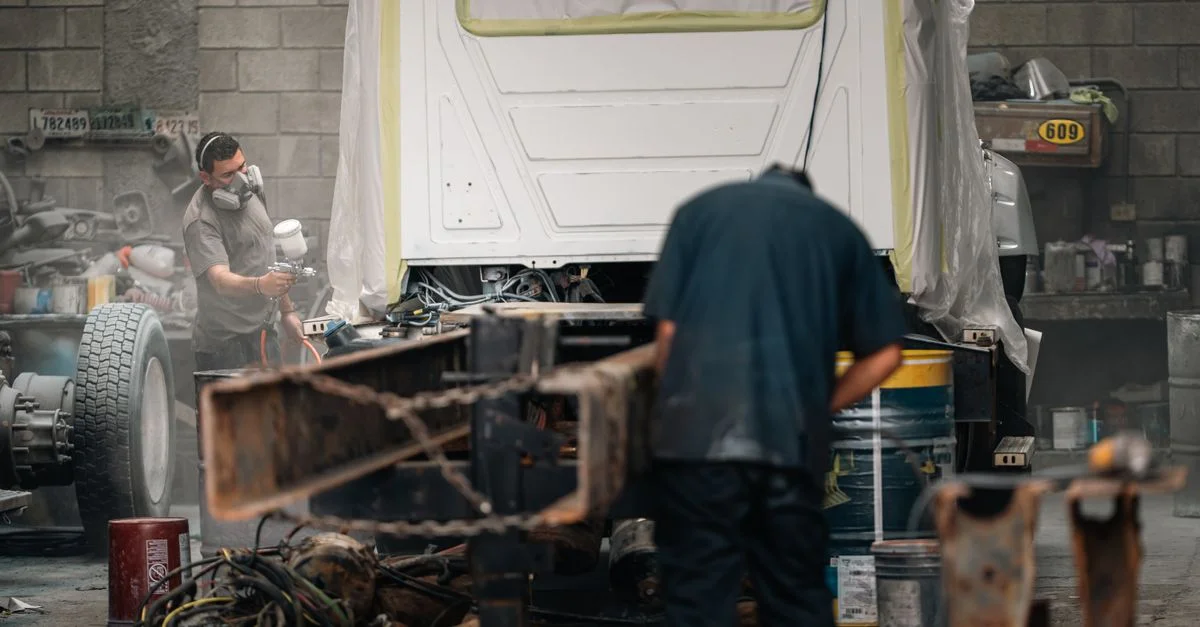 Deux ouvriers dans un atelier peignant un châssis de véhicule. Environnement industriel, équipement de protection.