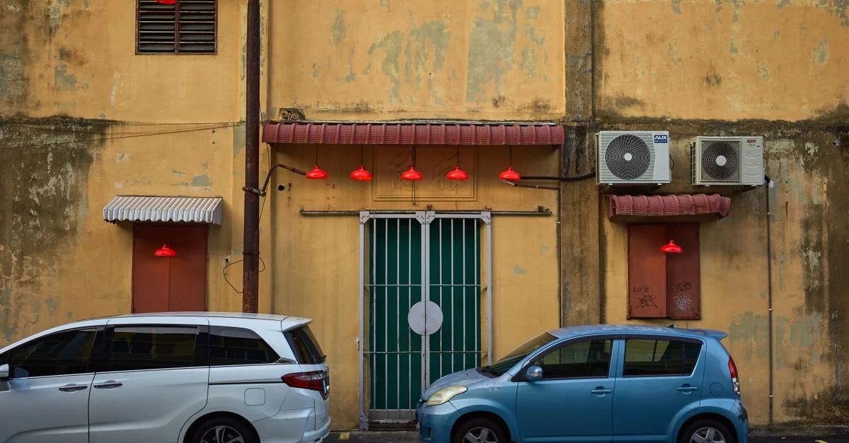 Scène urbaine colorée avec deux voitures garées devant un mur jaune vintage orné de lumières rouges et de climatiseurs.