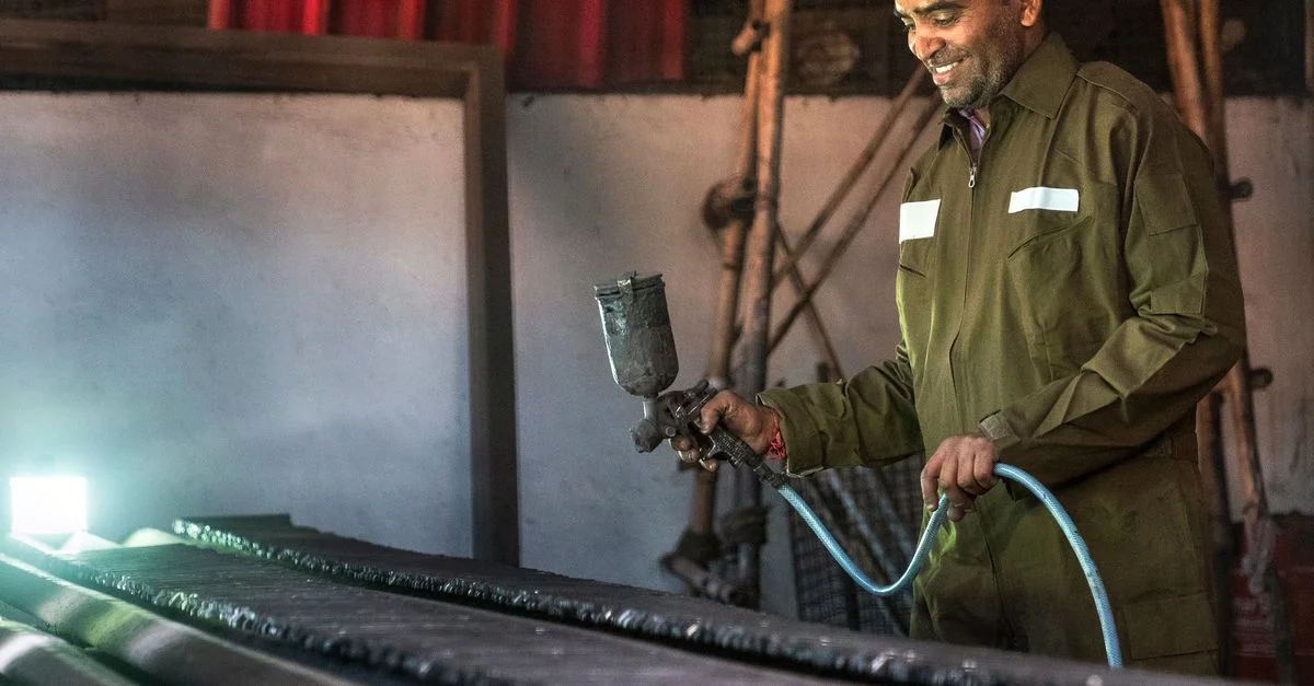 Homme souriant utilisant un pistolet à peinture dans un environnement d'atelier industriel.