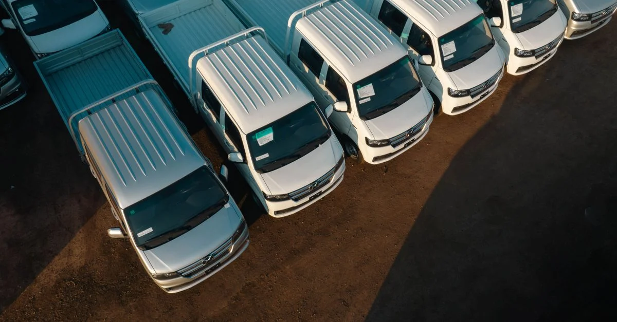 Vue aérienne de camionnettes blanches alignées soigneusement dans un parking. Éclairage à fort contraste.